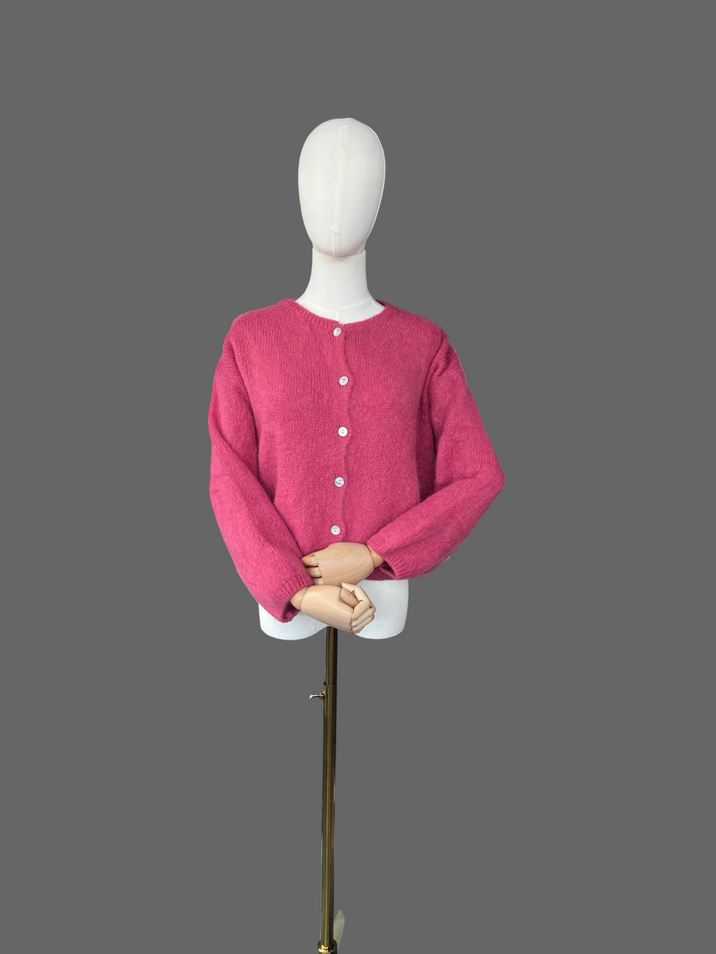 Mannequin wearing a pink cardigan in a room with a radiator and various items in the background.