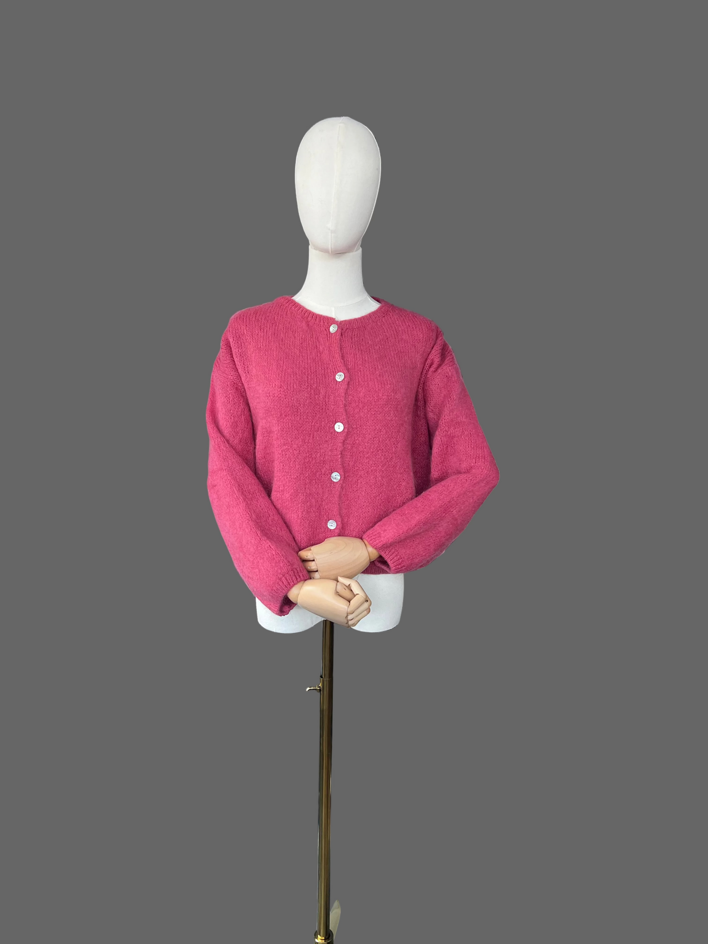 Mannequin wearing a pink cardigan in a room with a radiator and various items in the background.
