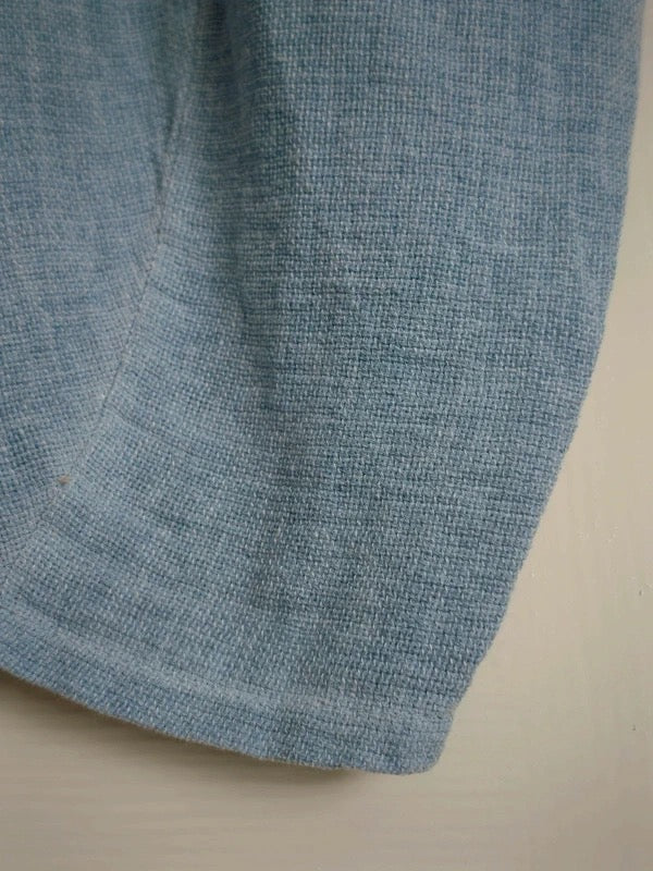 A close-up of a light blue heathered knit fabric, showing the textured weave and a folded hem, set against a plain off-white background.